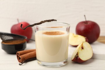 Delicious protein shake in glass, cinnamon, apples and vanilla pods on white wooden table, closeup
