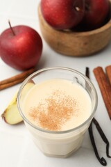 Delicious protein shake in glass, cinnamon, apples and vanilla pods on white table, closeup