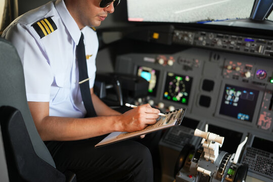 Handsome male pilots preparing flight documentation, checking paper flight plan, log book and air traffic before take off and landing. Or in simulator flight machine.