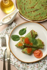 Tasty spinach crepes with salmon, avocado and red caviar served on wooden table, flat lay