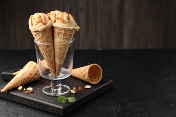 Tasty ice cream with caramel sauce in waffle cones on black table. Space for text