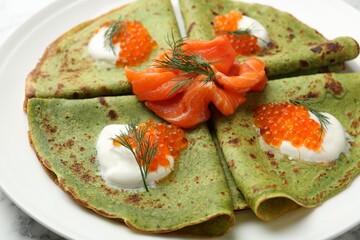 Tasty spinach crepes with salmon, red caviar, sour cream and dill on table, closeup