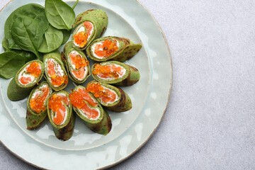 Tasty spinach crepes with salmon, cream cheese, red caviar and leaves on light grey table, top view. Space for text