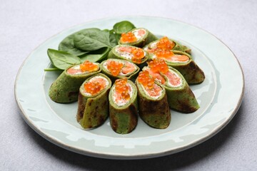 Tasty spinach crepes with salmon, cream cheese, red caviar and leaves on light grey table, closeup
