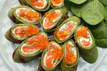 Tasty spinach crepes with salmon, cream cheese, red caviar and leaves on plate, top view