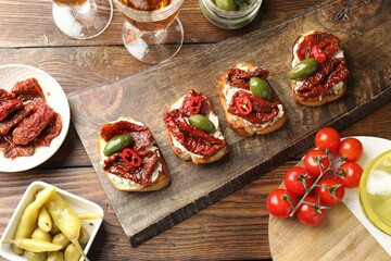 Delicious bruschettas with cream cheese, sun-dried tomatoes, chili pepper and green olives on wooden table, flat lay