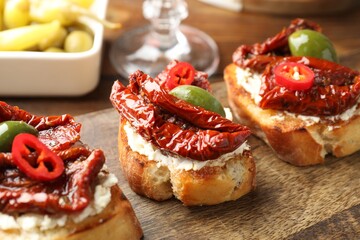 Delicious bruschettas with cream cheese, sun-dried tomatoes, chili pepper and green olives on wooden table, closeup