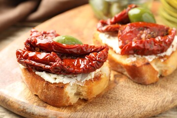 Delicious bruschettas with cream cheese, sun-dried tomatoes and green olives on table, closeup