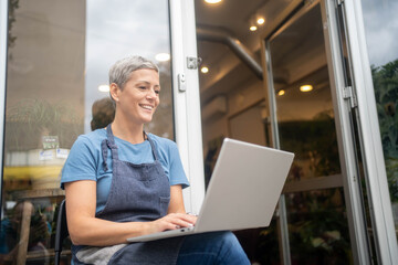Young female florist using laptop at flower shop counter.