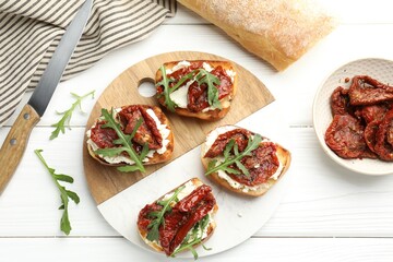 Delicious bruschettas with cream cheese, sun-dried tomatoes and arugula on white wooden table, flat lay