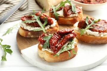 Delicious bruschettas with cream cheese, sun-dried tomatoes and arugula on table, closeup