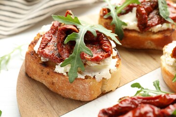 Delicious bruschettas with cream cheese, sun-dried tomatoes and arugula on table, closeup