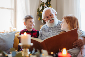 Small children with senior grandfather indoors at home at Christmas, looking at photographs.