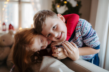 Small girl and boy in pajamas indoors at home at Christmas, playing.