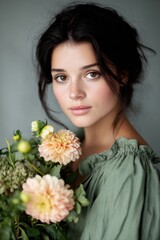 Fototapeta premium Woman with dark hair wearing green clothing holds a bouquet of flowers, showcasing natural beauty and elegance in a soft, serene environment with copy space