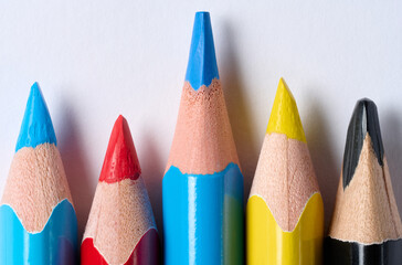 Close-up of the sharp tips of five colored pencils blue, red, yellow, black with visible wood grain and lead, arranged in a row