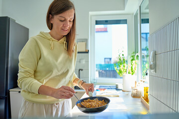 Woman standing in kitchen holding frying pan with cooked food