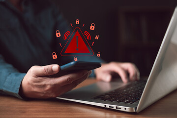 Man holding phone with red warning triangle icon. Cyber security concept of secure data protection failure. Hacking, phishing scam, and ransomware malware risk on laptop background.