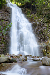 Fototapeta premium Stunning mountain waterfall captured with long exposure, creating smooth flowing water and highlighting natural textures, rocks, and surrounding greenery. Perfect for nature, landscape, or travel proj