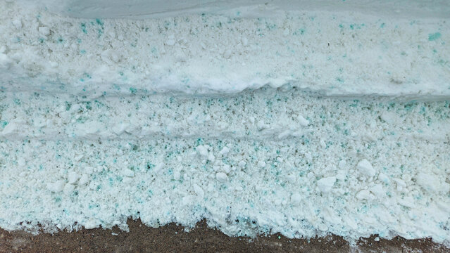 snow pile after clearing a walkway area, treated with a de-icing agent. Blue and green spots can be seen. Winter weather background.