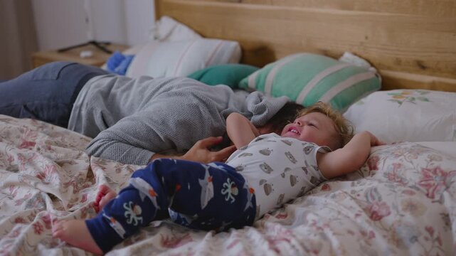 Toddler laughing on bed beside resting father in warm playful morning moment filled with joy movement affection and early day family tenderness inside cozy home environment