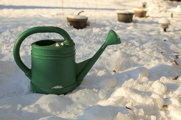 a large garden watering can in the foreground of a winter snow scene. the abrupt change of seasons. abstract weather background banner.
