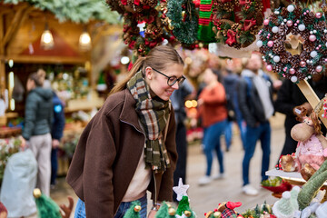 Cheerful young woman looking for New Year decorations in traditional street market