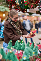 Cheerful young woman looking for New Year decorations in traditional street market
