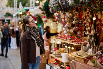 Cheerful young woman looking for New Year decorations in traditional street market