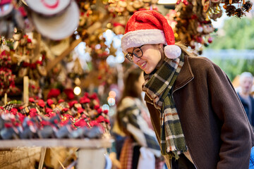 Cheerful young woman looking for New Year decorations in traditional street market
