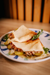 Savory crepes with minced meat, pickles and lettuce served on ceramic plate. Close-up composition with soft background and warm natural light
