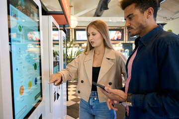 Couple using self service kiosk to order food in restaurant