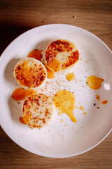Top view of cottage cheese pancakes served with fruit sauce and crumbs on white plate. Minimal flat lay composition, warm tones and cozy homemade breakfast aesthetic.