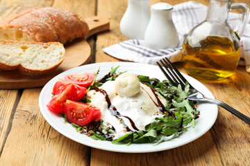 Delicious burrata cheese with arugula, tomatoes and dressing on wooden table, closeup