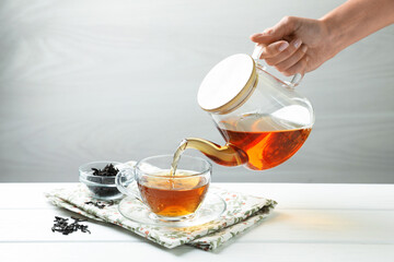 Woman pouring hot tea into cup from teapot at white wooden table, closeup. Space for text