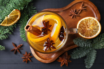 Delicious mulled white wine with slices of orange, spices and fir branches on black wooden table, flat lay