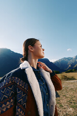 Fototapeta premium Woman portrait in the mountains hiking outdoors with backpack and jacket, enjoying sunlight and nature, travel adventure and serene landscape for leisure and exploration moments.
