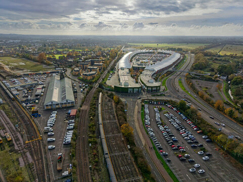Railway intersection in Ashford, Kent, UK. Aerial view of railway tracks passing cark park, warehouse and shopping center. Panoramic view of outskirts of Ashford town and landscape towards the sun.