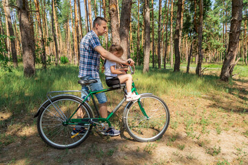 Obraz premium Dad rides his daughter in a bicycle seat in forest. A man carries a small child on a bicycle.