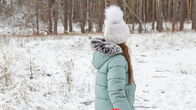 Cheerful positive child girl wearing a outerwear smiling walking through a snowy countryside forest