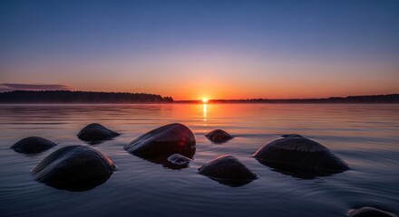 Tranquil dawn light bathes calm waters, showcasing smooth, dark boulders in a unique, captivating formation, reflecting the golden sunrise and serene sky, evoking peaceful wonder
