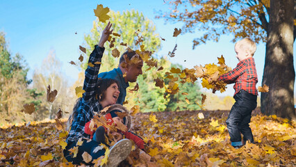 Playful family tossing autumn leaves, laughing together during golden sunlight in park landscape