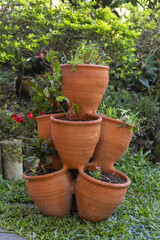 Stacked terracotta planter with various small plants and flowers on green grass, representing vertical gardening, outdoor decoration, and home horticulture.