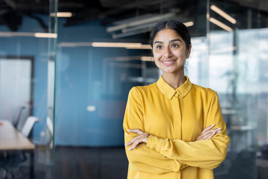 Portrait of a young successful and smiling Indian businesswoman standing in the office, arms crossed on her chest, looking confidently forward