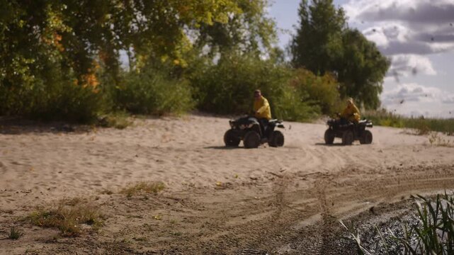 Riders on AVTs race shoreline, kicking dust across sandy riverbank with bluejacket leader carving tight turns while yellowjacket follower pushes