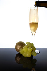 Serving champagne on classic glass next to Christmas ball and bunch of grapes
