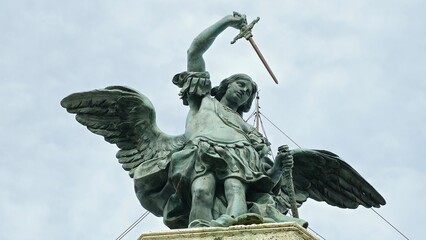 Rome, Italy - 12 January 2025. Archangel Michael’s statue crowns Castel Sant’Angelo, holding a sword skyward with wings extended against an overcast sky.