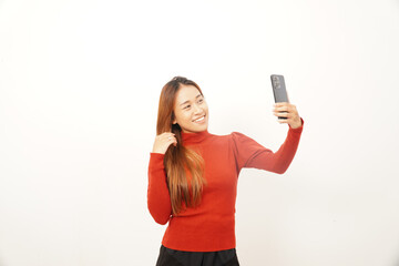 Happy young woman taking a selfie with her phone, smiling and adjusting her hair, engaging in social media activity