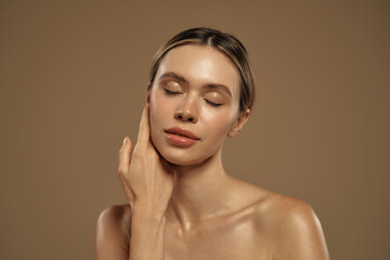 Close-up of young woman with glowing skin touching her chin