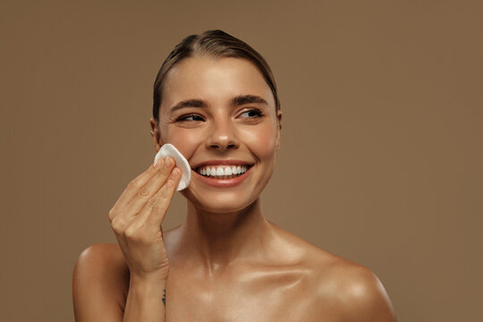 Beautiful woman smiling while cleansing her face with cotton pad